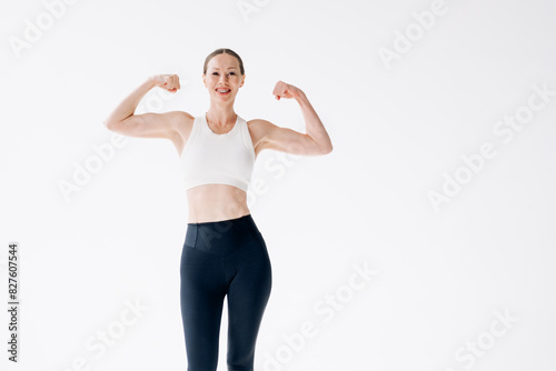A slender woman in sportswear and braces shows her biceps on a white background. Strong and energetic woman, copy space