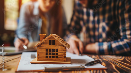 Real estate agent or realtor signing a mortgage agreement for a new home with a happy young couple. Home loan and property buying concept. Close-up of a miniature house.