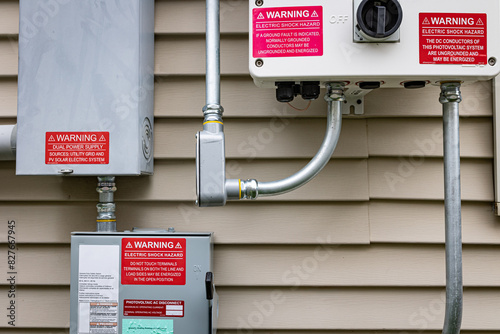 Close-up view of electricity boxes installed on the exterior of a single-family house: photovoltaic system inverter, quick disconnect box, and home electricity connection box.