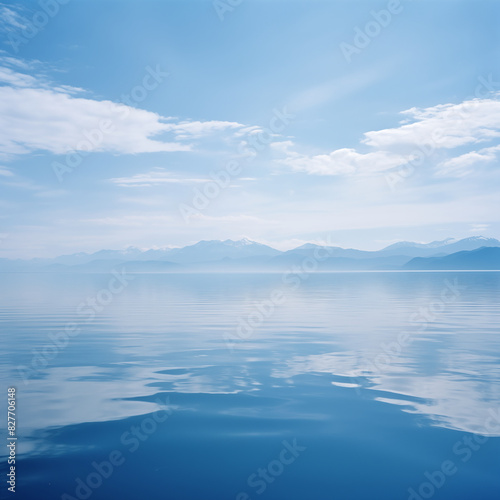 A calm lake with mountains and white clouds in the distance