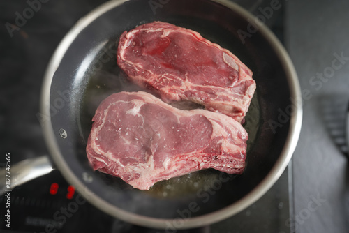 Close-up of raw ribeye steaks cooking in a pan, showcasing the texture and marbling, ideal for food-related content, culinary guides, and steak preparation techniques
