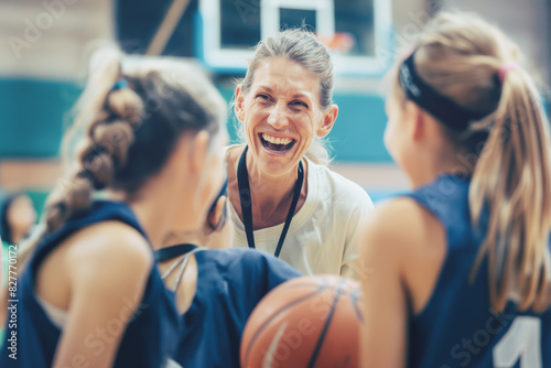 Laughing basketball coach with young female players during practice in gym. Joyful and energetic environment fostering teamwork and enthusiasm