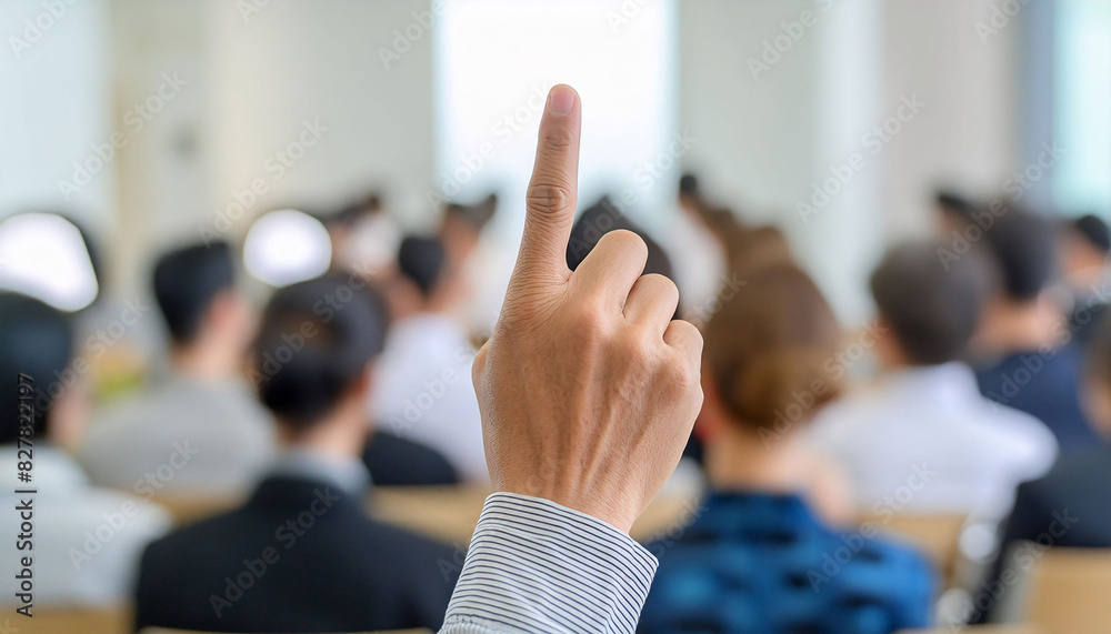 Raised hand with the index finger upwards in a conference room, active participation engagement. Raised hand with the index finger upwards in a conference room, active participation engagement.