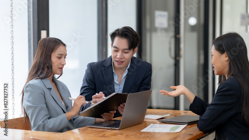 A group of business professionals having a meeting in a modern office setting. They are engaged in a discussion with documents and a laptop.