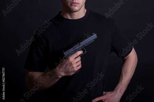 Young man in a black t-shirt holding a pistol on a dark background