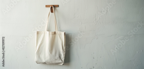 A reusable fabric tote bag hanging on a simple wooden hook against a plain white wall, symbolizing International Plastic Bag Free Day.