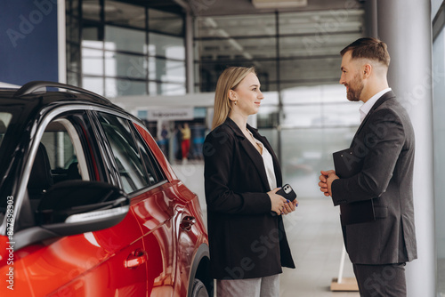 Car Sales Manager Showing Auto To Caucasian Lady Buyer Standing In Luxury Automobile Dealership Store. Buying Vehicle Concept © anatoliycherkas