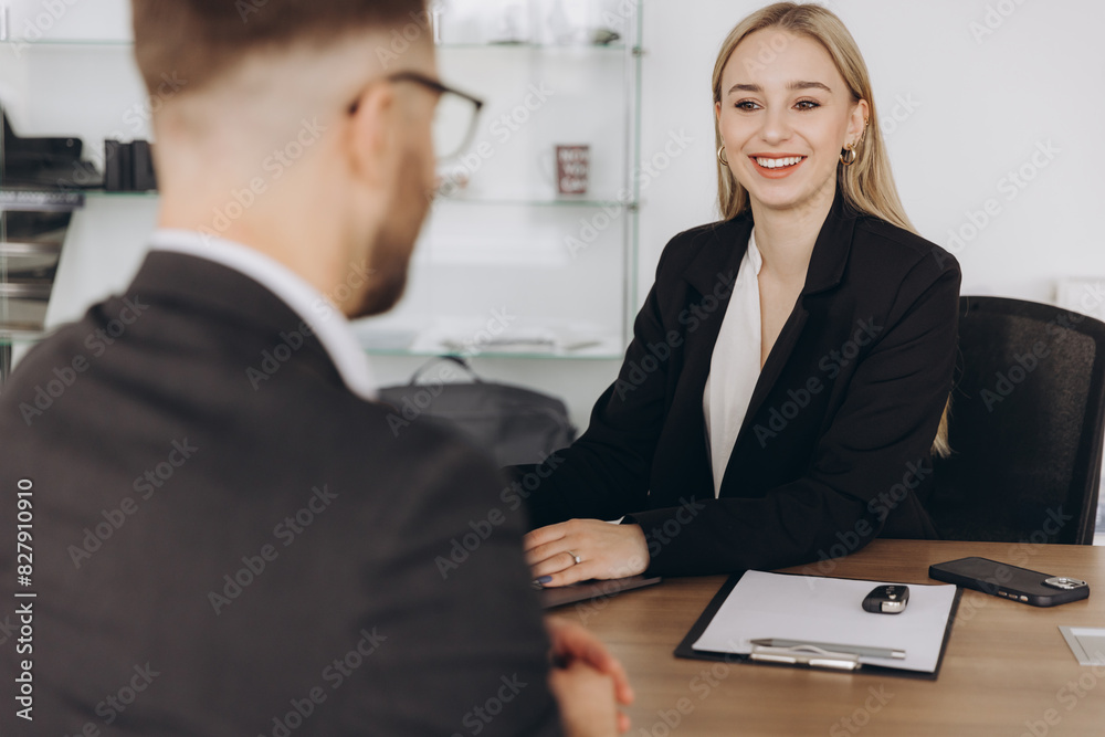 Smiling happy female manager car salesman in car dealership signing contract at table with male buyer in suit Smiling happy female manager car salesman in car dealership signing contract at table with male buyer in suit