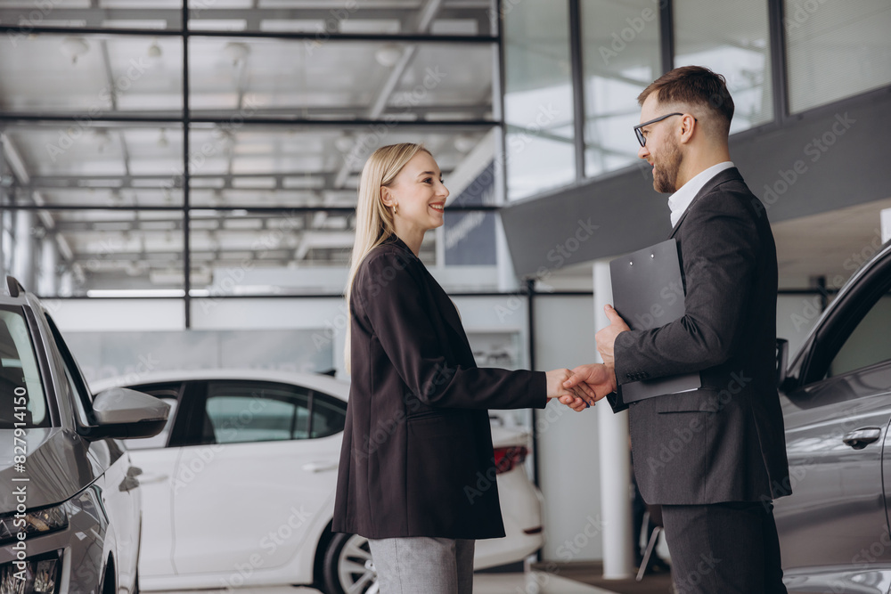 Happy woman buying a car and closing the deal with a handshake with the salesman at the dealership Happy woman buying a car and closing the deal with a handshake with the salesman at the dealership
