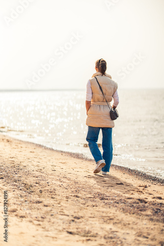 Back view of woman walking along the beach looking at the sun. Vertical shot.