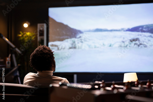 Cord cutter mesmerized by online nature clips with beautiful cinematography on widescreen smart TV display. BIPOC man enjoying scenery shots of snowy landscape filled with ice on VOD channel