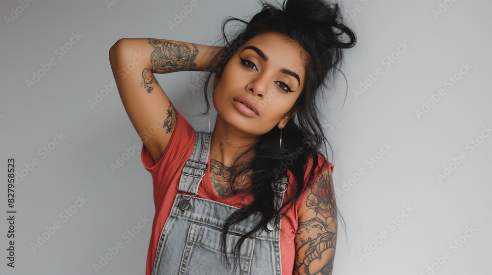 Beautiful young Indian woman with tattoos wearing overalls posing while looking at the camera against a white background Beautiful young Indian woman with tattoos wearing overalls posing while looking at the camera against a white background
