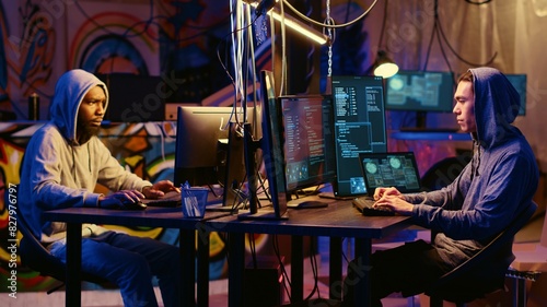 Hacker group members working together in hidden place with graffiti walls, deploying malware on unsecured computers to steal sensitive and private information from internet users