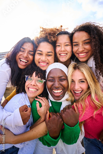 Vertical of group of beautiful young multiracial girl friends community hugging and looking at camera outdoor. Smiling only women together embraced affectionately. Female friendships and quality time