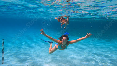 Fotografi UNDERWATER: Beautiful woman in bikini dives under her dog that swims on the surface of crystal clear sea