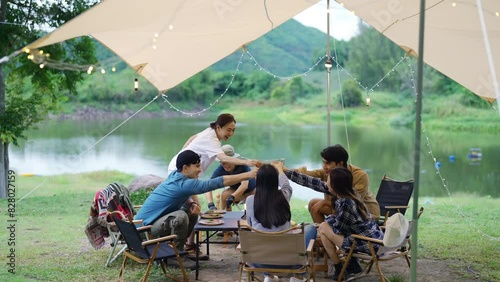 Group of Happy Asian man and woman enjoy and fun outdoor lifestyle travel nature camping in forest on summer vacation. People friends having dinner eating bbq grill and drinking beer together at night