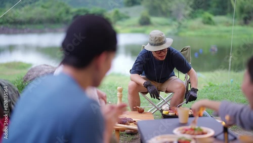 Group of Happy Asian man and woman enjoy and fun outdoor lifestyle travel nature camping in forest on summer vacation. People friends having dinner eating bbq grill and drinking beer together at night photo