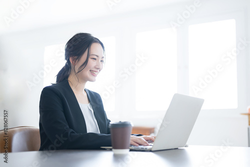 逆光の綺麗なオフィスでパソコンを使いタイピングをする女性の上半身アップのビジネスシーン　コピースペースあり