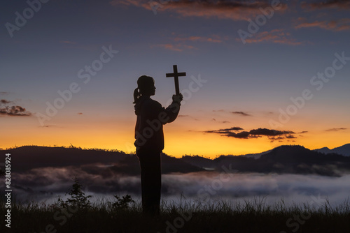 Silhouette girl holding a holy cross praying on sunrise background, Crucifix, Symbol of Faith.
