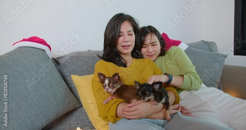 Happy Loving Asian lesbian couple lgbt smiling embracing together while sitting on the couch at home. couple holding petting cute chihuahua dog relaxing on sofa. lgbt relationship pet love	

