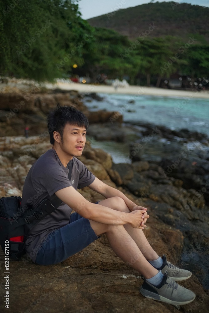 asian man sitting on the rocks looking toward the sea asian man sitting on the rocks looking toward the sea