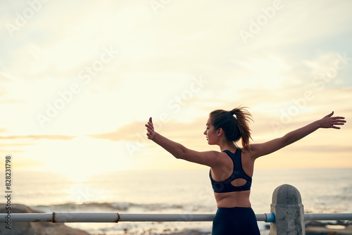 Back, woman and arms in air for sunset at beach for fitness, exercise and freedom in summer. Celebration, runner and success in nature for workout, training and ocean with achievement for wellness