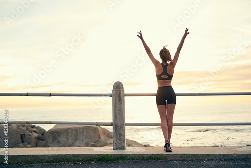 Back, woman and sunset with arms in air at beach for fitness, exercise and freedom in summer. Female runner, celebration and wellness in nature for workout and training at ocean with achievement
