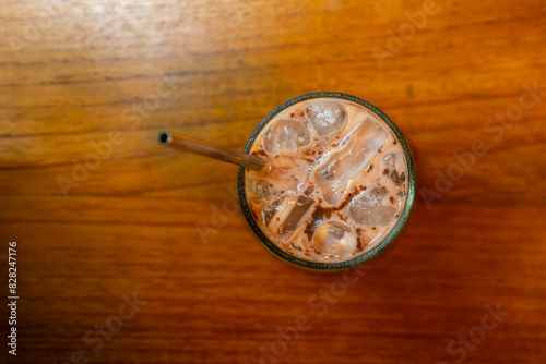 iced hazelnut and chocolate milk drink served on transparent glass, over small wooden plate, on wooden table surface