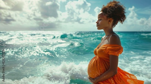 Pregnant woman in orange dress standing on the beach and looking at sea