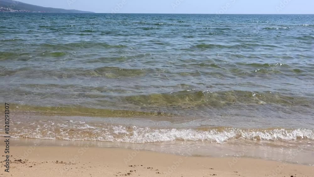 Tranquil scene of small waves lapping at a sandy shore with a clear blue sky Tranquil scene of small waves lapping at a sandy shore with a clear blue sky