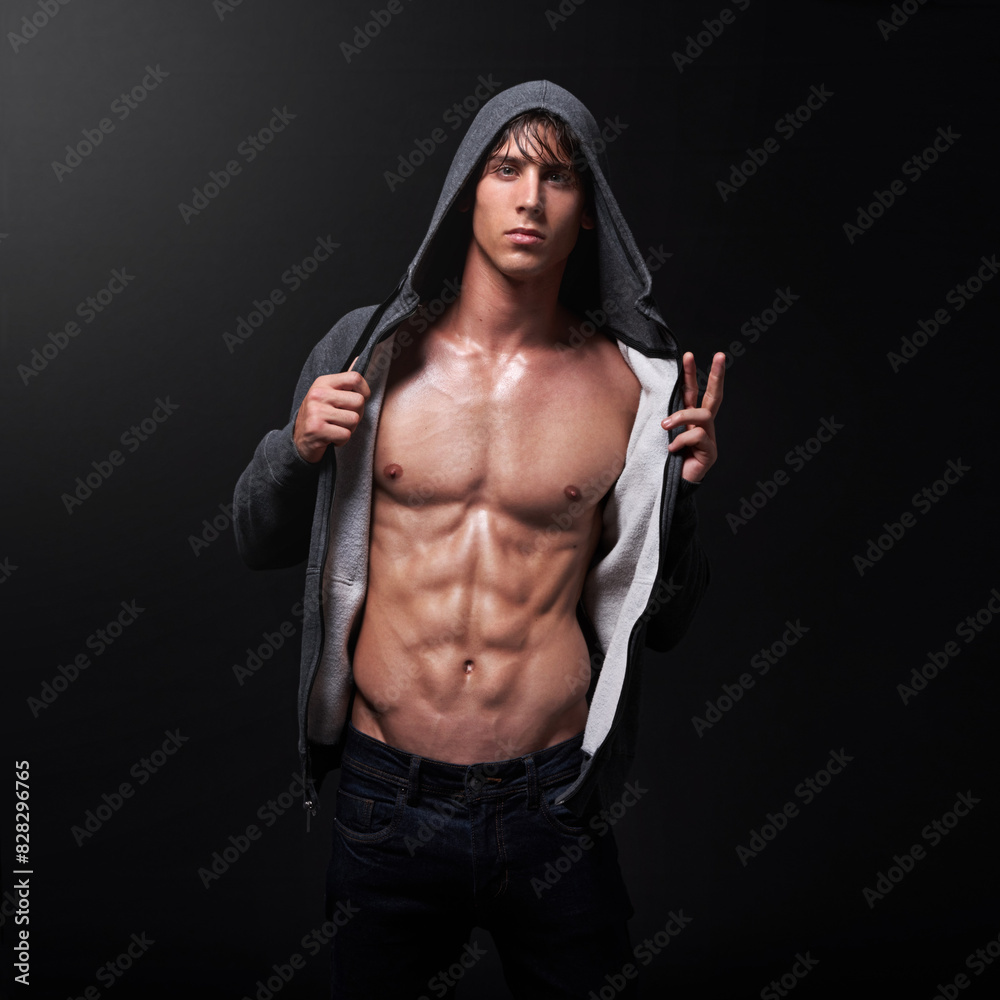 Obraz premium Confident, bodybuilder and portrait of man in studio for muscle, healthy body and pride in fitness. Male person, athlete and serious with hoodie for sports, six pack and wellness on black background