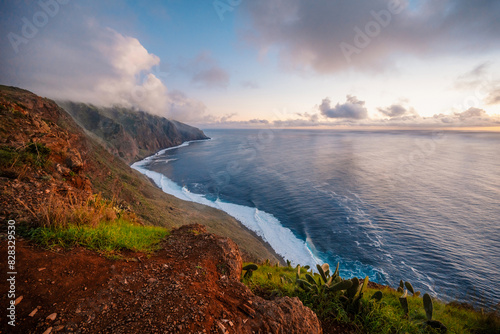 View of rough ocean with waves, volcanic beach, sunset over a huge cliff  in Lighthouse Ponta do Pargo, Madeira, Portugal photo
