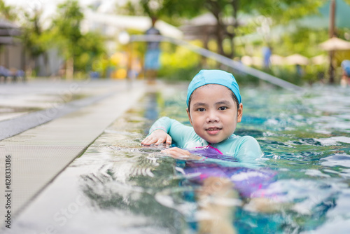 swimming pool with Asian child smile or kid girl wearing swimsuit and cap on edge pool to happy fun in waterpark or person learning swim to sports exercise on summer school or holiday travel at hotel