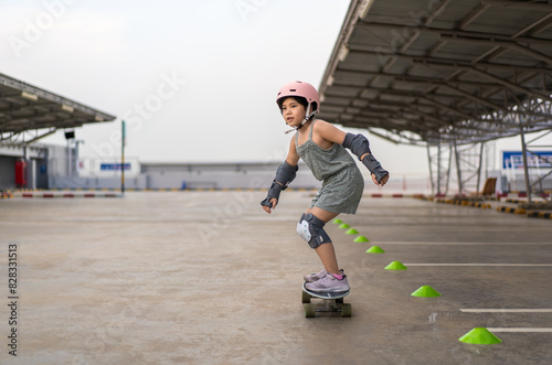 asian child skater exercise or kid girl fun playing surf skate or skateboard by turning practice cones in skatepark to sports extreme at parking to wearing body safety helmet elbow wrist knee guard