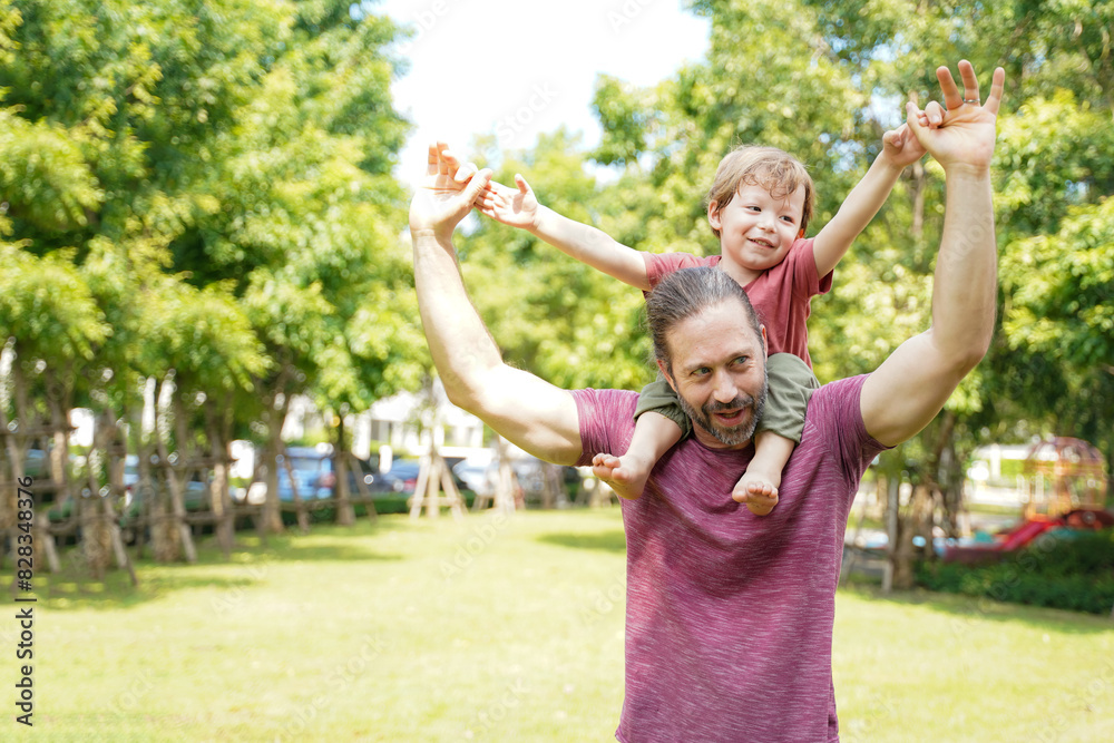 Obraz premium Happy Family. Happy little boy stretching out hands while his father carrying him cheerful and enjoying in the garden park. Father and boy relax and chill outdoor on summer day