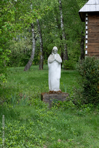 A Damaged, Old Statue of the Mother of God, Abandoned in the Cemetery Dump, Trees with Green Leaves in the Background.