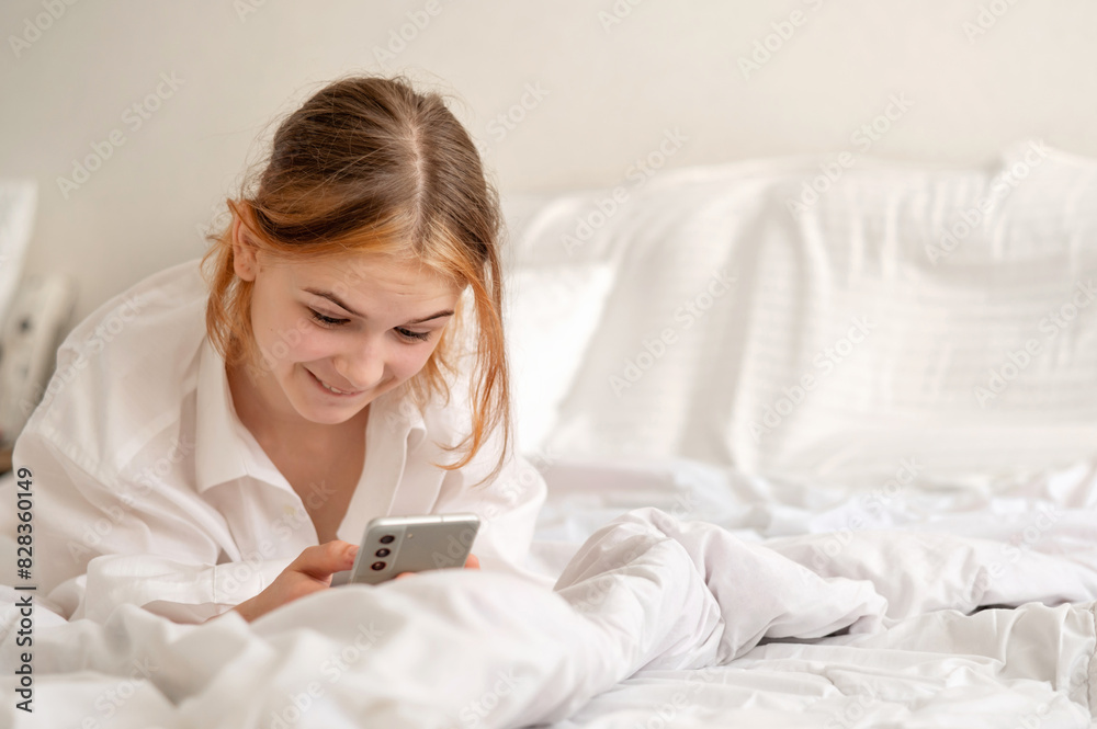 Curious teenage girl with funny face expression using mobile phone laying in bed, looking at mobile screen, neutral white Nordic bedroom interior, lifestyle Curious teenage girl with funny face expression using mobile phone laying in bed, looking at mobile screen, neutral white Nordic bedroom interior, lifestyle