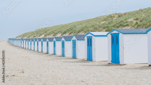 A charming row of blue and white beach huts standing tall on the sandy shores, creating a picturesque scene against the clear blue sky. De Koog beach Texel