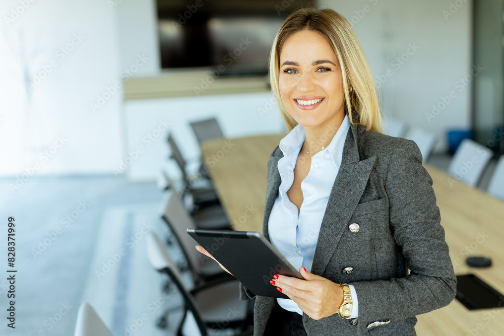 Smiling professional woman in red blazer holding tablet in modern conference room during daytime Smiling professional woman in red blazer holding tablet in modern conference room during daytime