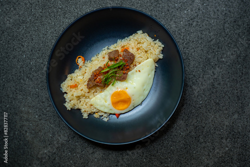 beef saikoro rice bowl and sunny side up egg on black plate, over stone tile photo