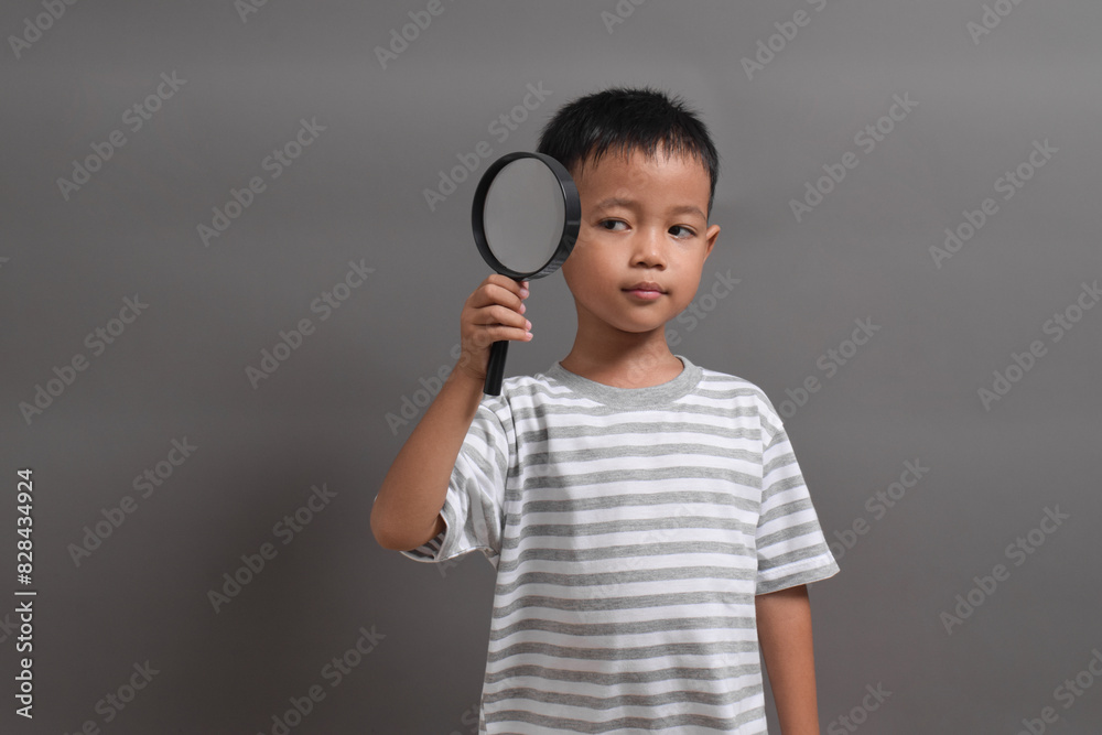 Image of Asian child posing using a magnifying glass on grey background Image of Asian child posing using a magnifying glass on grey background