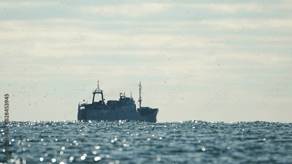 Fishing boat trawler catches fish while sailing on sea. A commercial fishing boat on the horizon in a distance sail to catch school of fish on calm sea surface in summer. Commercial catch of sea fish.