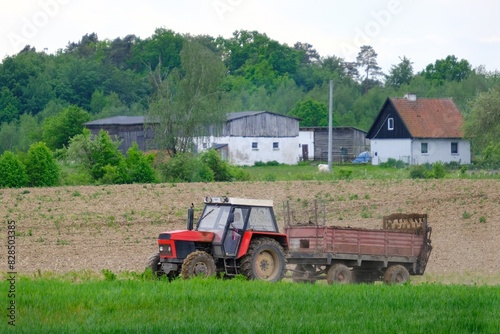 A red tractor with a trailer drives through a plowed field