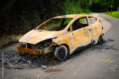 front side view of a rusty orange burnt out car on a concrete public footpath 