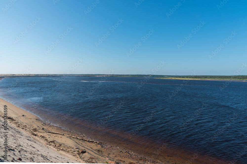 panoramic view of a wide river with sandy shores and a forest far away panoramic view of a wide river with sandy shores and a forest far away