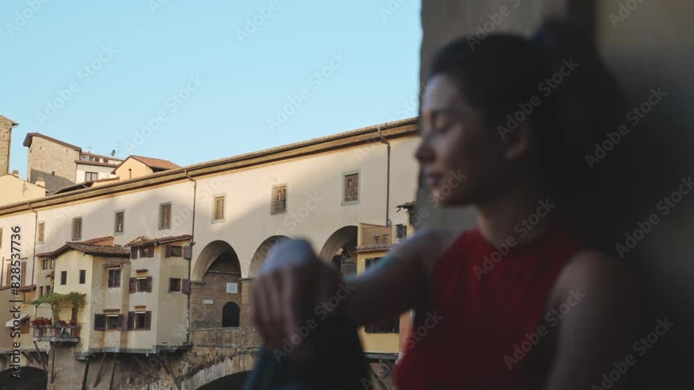Charming asian woman wearing red T-shirt and striped blue jeans relaxing on Vecchio bridge. Portrait of pretty girl looking into the distance and thinking about beautiful and pacifying. Charming asian woman wearing red T-shirt and striped blue jeans relaxing on Vecchio bridge. Portrait of pretty girl looking into the distance and thinking about beautiful and pacifying.