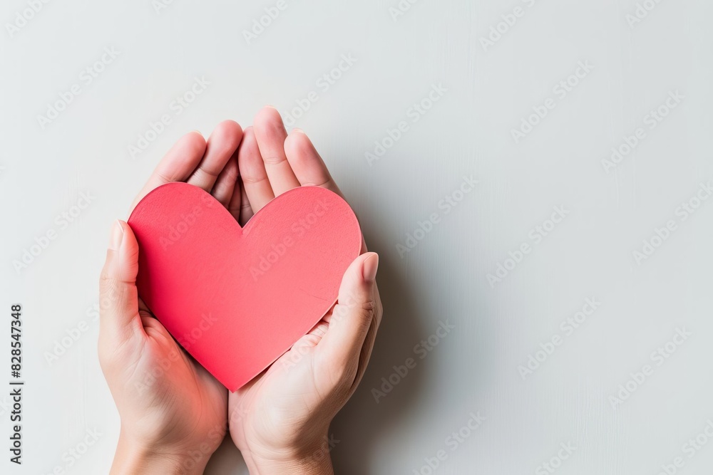 Fototapeta premium Hands holding a red heart on a white background, symbolizing love, care, and kindness, perfect for health and wellness themes.
