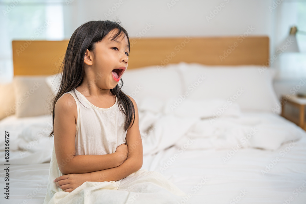 Portrait of sick unhappy little child asian girl touching belly stomach with suffering from stomach ache pain, gastritis, gastroenteritis, food poisoning, diarrhea, intestinal inflammation at home Portrait of sick unhappy little child asian girl touching belly stomach with suffering from stomach ache pain, gastritis, gastroenteritis, food poisoning, diarrhea, intestinal inflammation at home