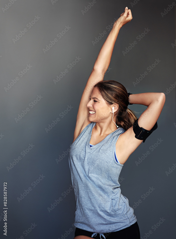 Fitness, stretching and woman in studio with arm raised for gym goals, achievement and earphones. Winning, power and strong athlete girl with tech, music and healthy body builder on grey background Fitness, stretching and woman in studio with arm raised for gym goals, achievement and earphones. Winning, power and strong athlete girl with tech, music and healthy body builder on grey background