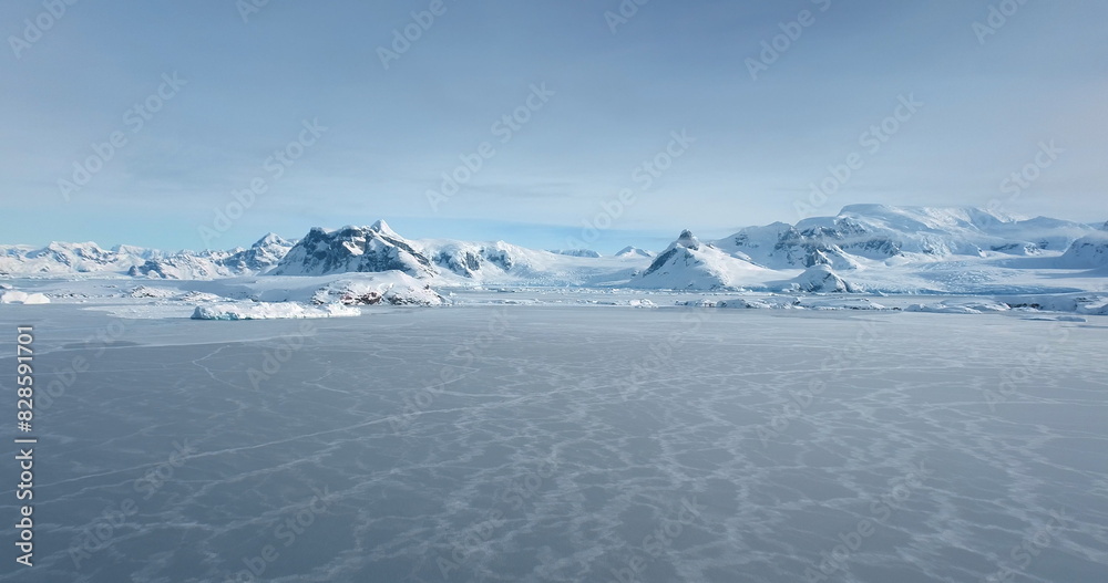 Obraz premium Snowy landscape with majestic mountains in background. Aerial fly over frozen polar ocean in Antarctica, covered snow wild desert land. Beautiful winter scene, wild nature wallpaper. Travel to Arctic
